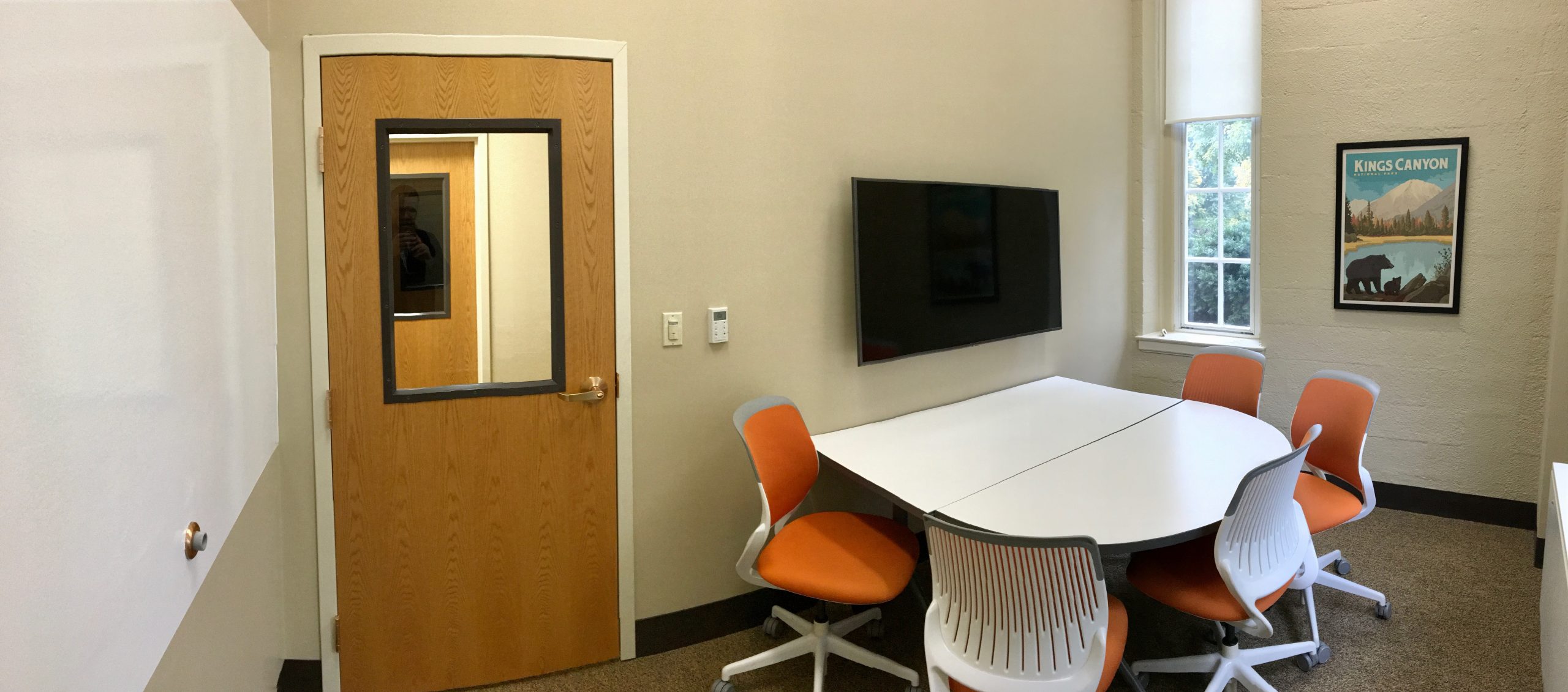 A study room with a table, mounted screen, whiteboards, and five chairs