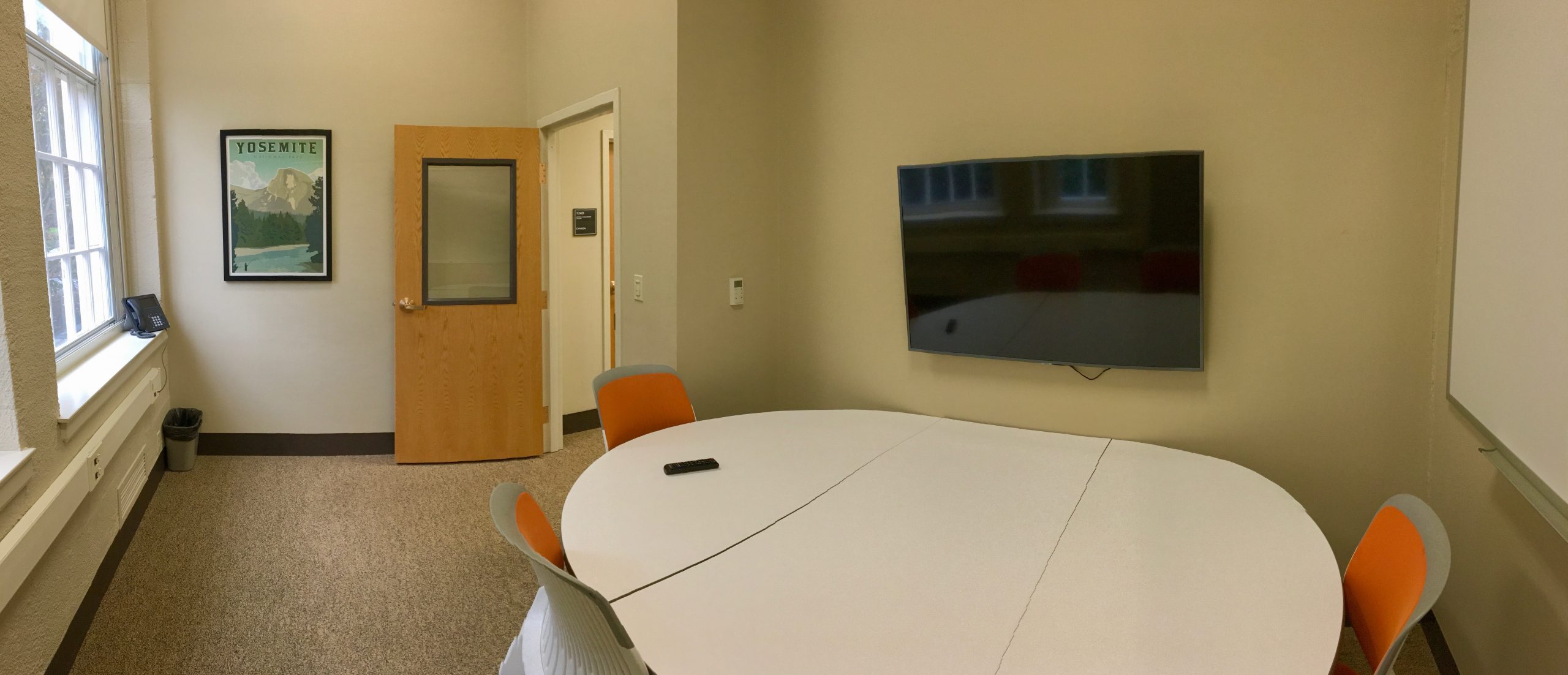 A study room with a table, white board, mounted screen, and four chairs