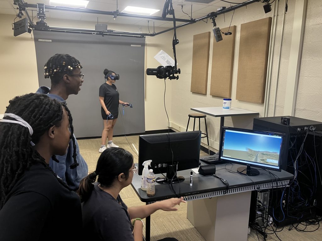 Gianna using a VR headset in the nd Library 2nd Floor Studio while Thandeka, Jackline, and Malika watch the monitor.