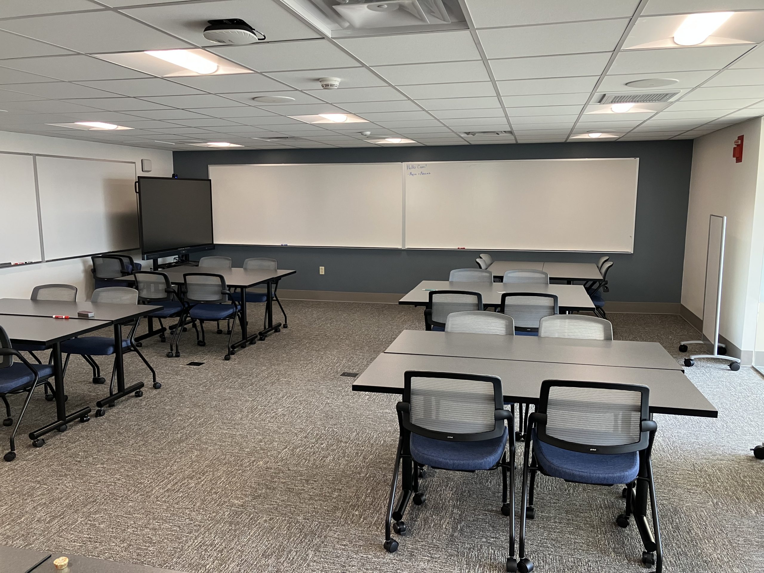 A classroom space with large whiteboards, movable tables and chairs, and a large mobile touchscreen.