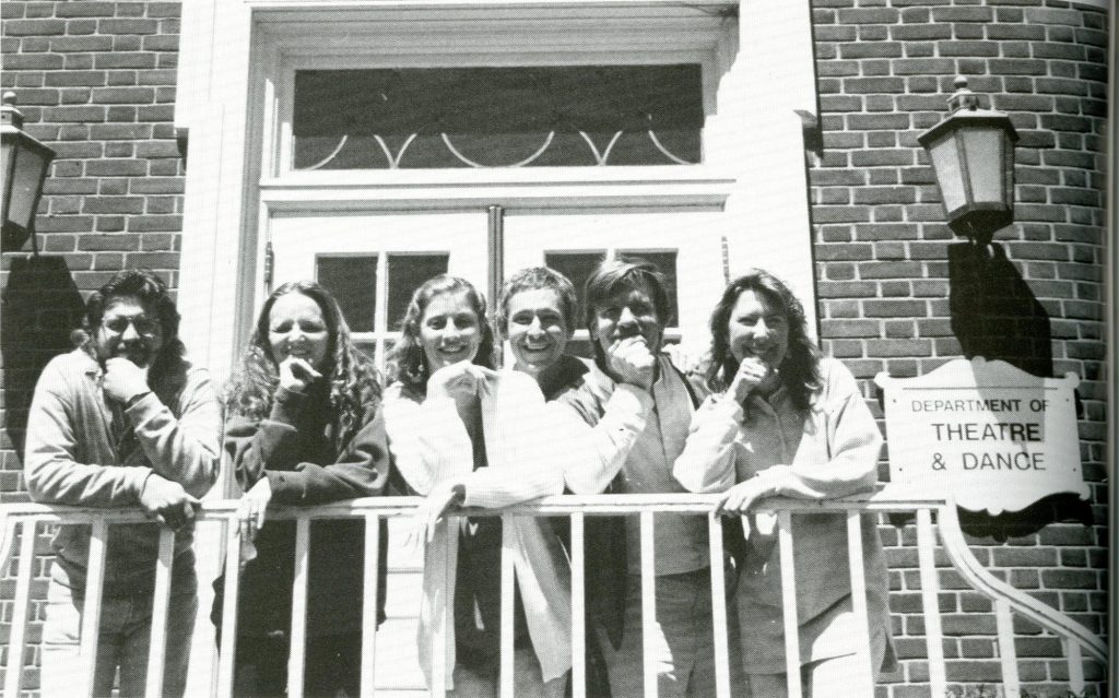 A row of Theatre and Dance faculty learning against a railing next to a sign on the building that says, "Department of Theatre and Dance."